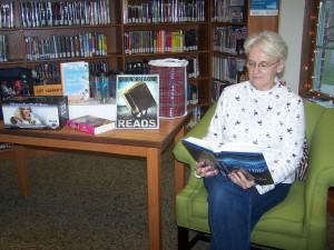 Carol Haab reads one of her favorite books by the table of prizes available for Milford Public Library's Adult Reading Club winners.  Adult Reading club begins Jan. 2 and lasts until March 30.  Sign up at the adult department desk after the first of the year and you could win one of these prizes! 