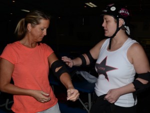 Stacey Page, left, gets a lesson in padding up for roller derby action from Lake City Roller Doll Megan "Mouthy Megpie" Dinse. (Photo by Alyssa Richardson)