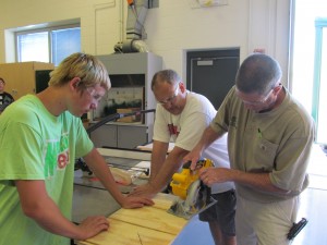 Student Drew Denney, left, watches as Ed Waltz, right, building trades instructor for Wawasee High School, uses a saw. In the middle is Jamie McAdams, WHS industrial arts teacher. As part of the Early Career Options Summer Challenge, at-risk students helped build a shed for Habitat for Humanity. (Photo provided