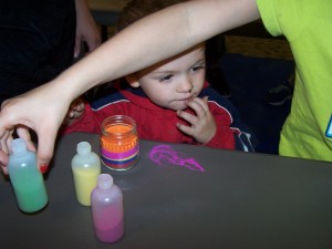 David Owens, with his sister's help, makes sand jar art with a baby food jar and colored sand at the Milford Public Library.