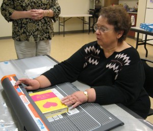 Cataloguer Paula Markly demonstrates the Library’s new book covering machine that enables the staff to cover books much more quickly than by hand. Now new books can be put on the shelves and available to patrons much sooner. (Photo provided)