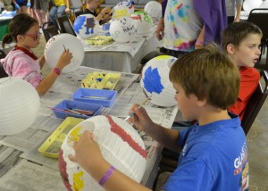 In front camper Shane Miller works on his Flash paper lantern, having painted the superhero’s face on one side. His fellow campers, in back, Mercy Lederach, left, and Jason Dady work on their own lantern projects.