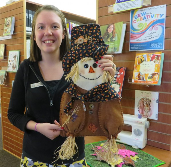 Library Clerk Tiffany Weisser holds the cute scarecrow craft that patrons can learn to make at the Craft-A-Scarecrow Workshop on Wednesday, Oct. 1, at 1:00.  To attend the workshop, sign up at the front desk.