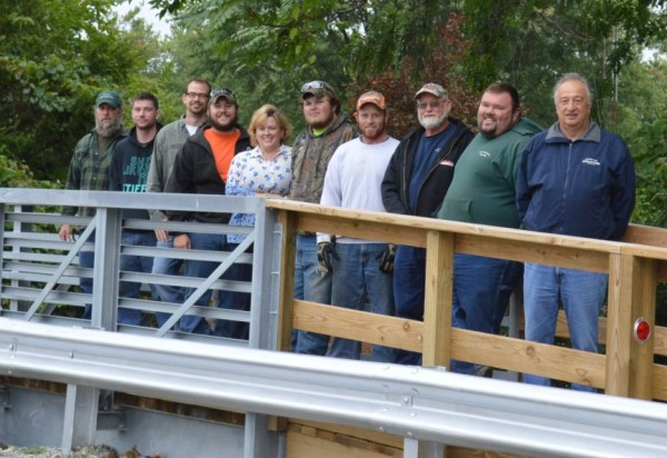 Shown are members of the Syracuse Street Department who worked on constructing the pedestrian bridge on Harkless Drive. Construction was started in May and completed in mid-July. From left are Paul Hoffman, street foreman; David Miller, Jeremy Sponseller, public works director; Zach Goodyear, Holly Swoverland, representing K-21 Foundation; Jared Hoover, Seth Hall, Ken Plikerd, John “Tiny” Reynolds and Town Manager Henry DeJulia.