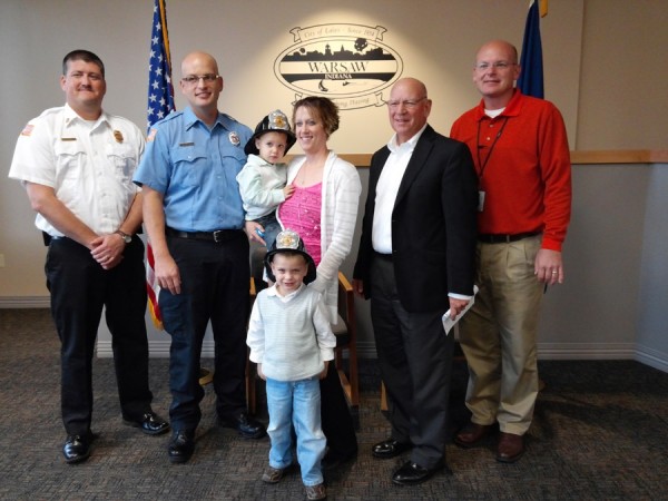 Troy Knefelkamp was sworn in Monday morning as the newest firefighter with the Warsaw-Wayne Fire Territory. Shown in front is his son Leighton. In back are Chief Michael Brubaker, Knefelkamp, Nicole Leighton holding Maxton Knefelkamp, Charles Smith and Jeff Grose, board of public works members. (Photo by Deb Patterson)