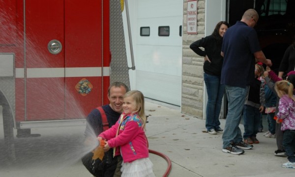 Audrey Fitzsimmons proudly sprays the sidewalk while practicing with the firehose, under the direction of firefighter Gavin Foster. Fitzsimmons traveled with her preschool group to Milford Fire Department and learned techniques like “stop, drop and roll,” along with emergency phone numbers, and exiting the house safely if a fire were to occur.