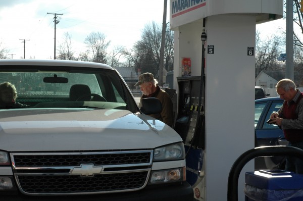 Cliff Wolf (left) tops off his tank Monday while Don Schmucker begins his transaction at the Marathon station in Milford. The station recently joined a growing list of outlets lowering their price for regular unleaded to below $2 a gallon.