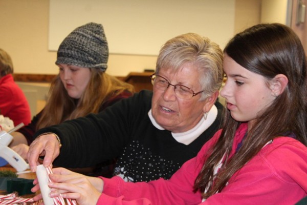 Glue guns were used to make candy cane candles at the Syracuse Library on Dec. 2. Lila Fiereck is shown making her decoration with Linda Weybright, one of the volunteers from the Homemakers Club. Emelia Layne is working on her candle behind Weybright.   