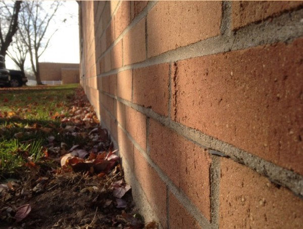 The foundation near the entrance of the school is between 1-2 inches off from the wall. 