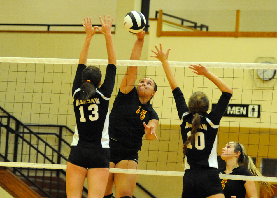 Elkhart Memorial's Darrian Mowery hammers home a kill between the block attempt of Warsaw's Caroline Mayer (13) and Lexie Day (10) Tuesday night. (Photos by Mike Deak)