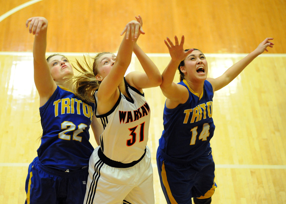 Warsaw's Kacy Bragg follows through on a shot attempt as Triton's Nicole Sechrist (22) and Jaela Meister (14) converge.