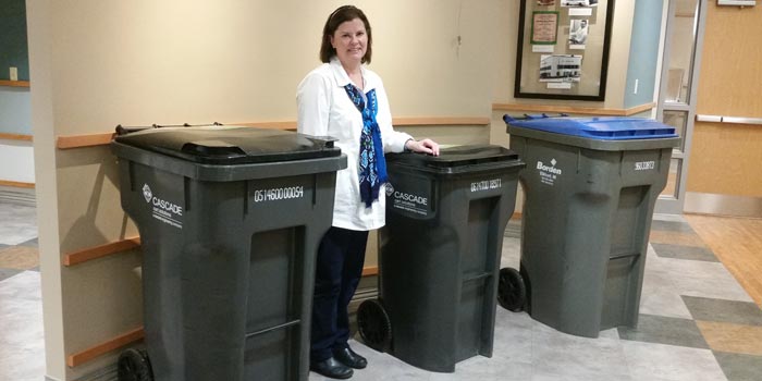 Mary Lou Plummer shows off Warsaw's new trash collection bins. The bin with the blue lid is an example of the current recycle bins. (Photo by Amanda McFarland)