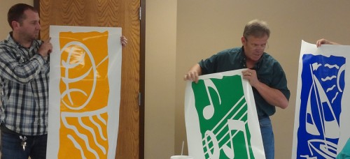 Shawn Gardner, maintenance diretor; Larry Plummer, park superintendent; and Sheila Wieringa, recreation director, hold up three banners which have the three elements of the department's logo: sports, music and recreation.