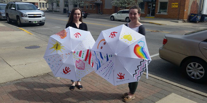 Katie Yocum, left, and Abigail Smith show off umbrellas decorated by twin sisters Katherine and Caroline for the upcoming Parasol Parade for Cure JM. (Photo by Amanda McFarland)