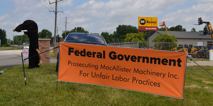 Representatives of the Local 150 sit next to a sign outside MacAllister Equipment, Warsaw. (Photo by Amanda McFarland)