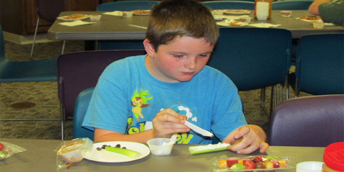 Andrew Bradley makes his snack Ant on a Log with Raisins, Celery, and Cream Cheese at our First Food and Fun Session on June 15 where kids learned how to make healthy treats!
